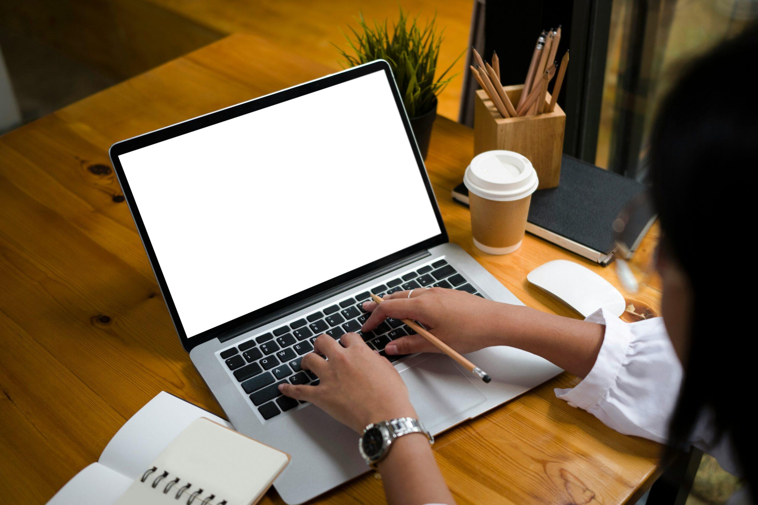 Person working on laptop at wooden desk with blank screen, notebook, and coffee cup — representing online legal consultation or digital case submission