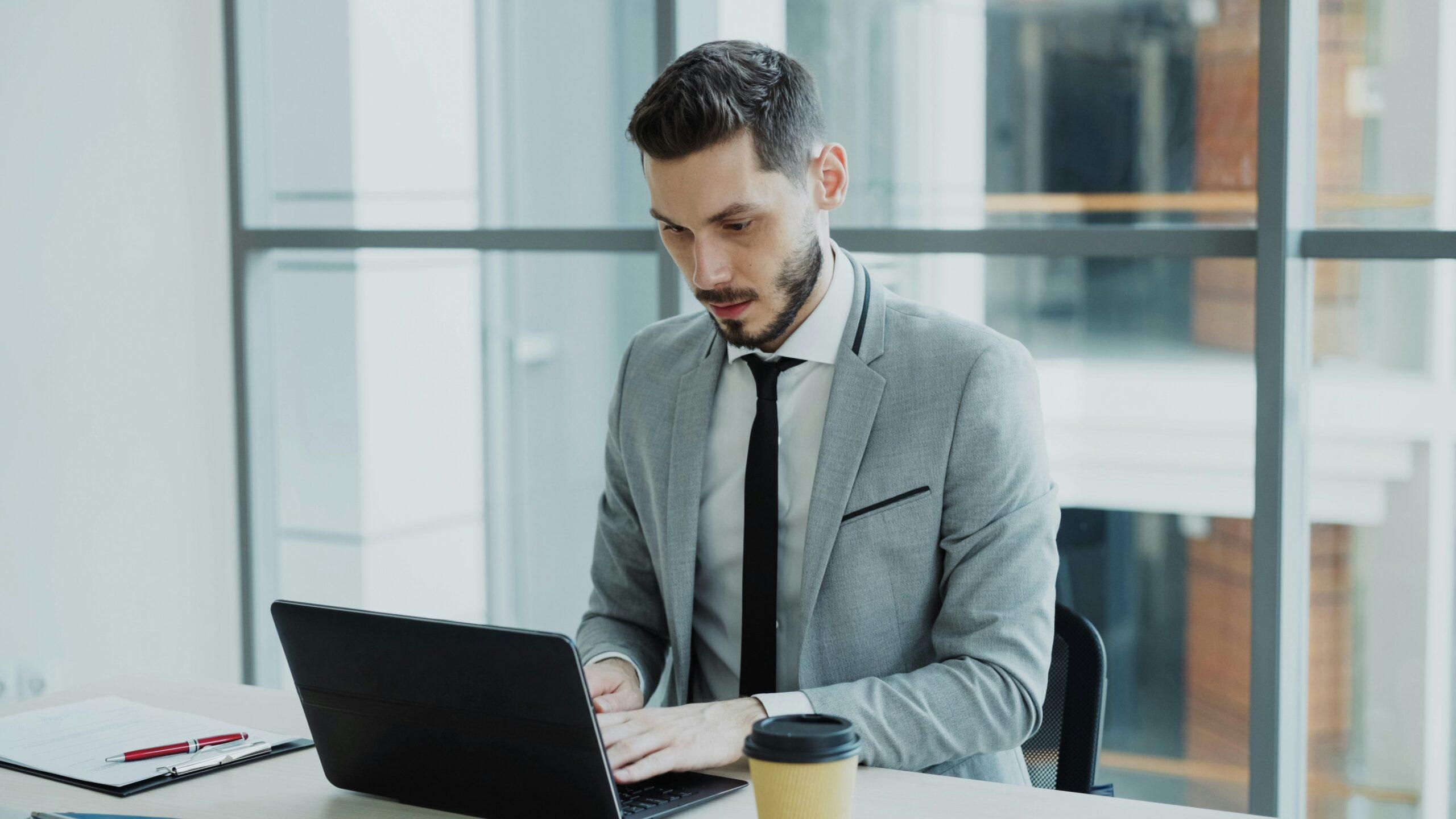Male lawyer in gray suit working on laptop in modern office, focusing on legal research and case documentation