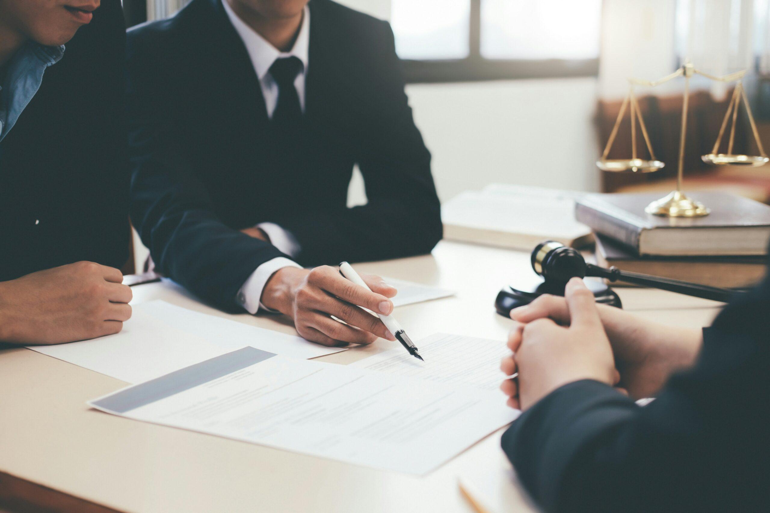 Three business professionals seated at a table, engaged in discussion with a pen and paper in front of them.