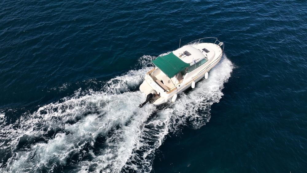 Aerial view of a white cabin cruiser with a green canopy speeding across dark blue water, leaving a wake.